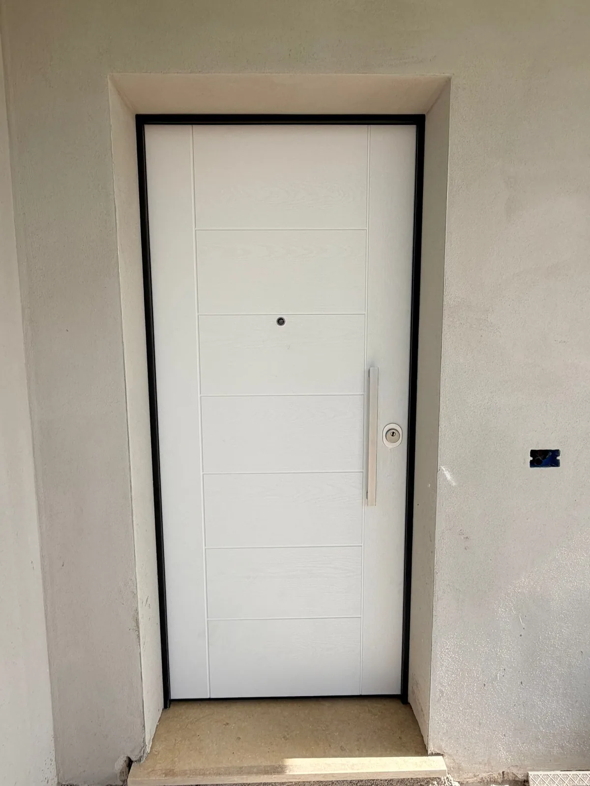Porta blindata bianca a doghe orizzontali con maniglione verticale e telaio scuro, vista dall'esterno