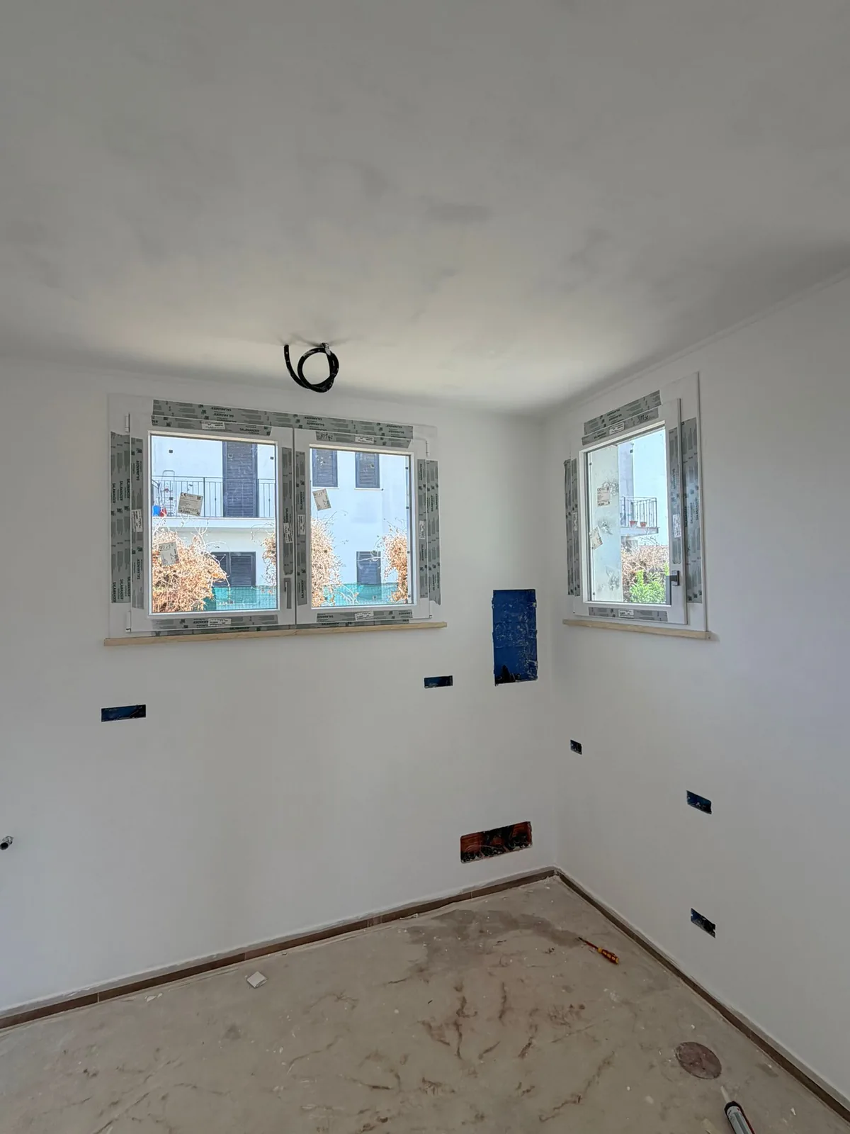 Stanza al grezzo con due finestre in PVC bianco appena posate, pellicole protettive sui telai