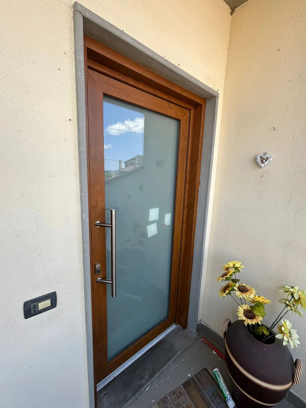 Porta d'ingresso con pannello in vetro smerigliato, telaio color legno e maniglione verticale in acciaio