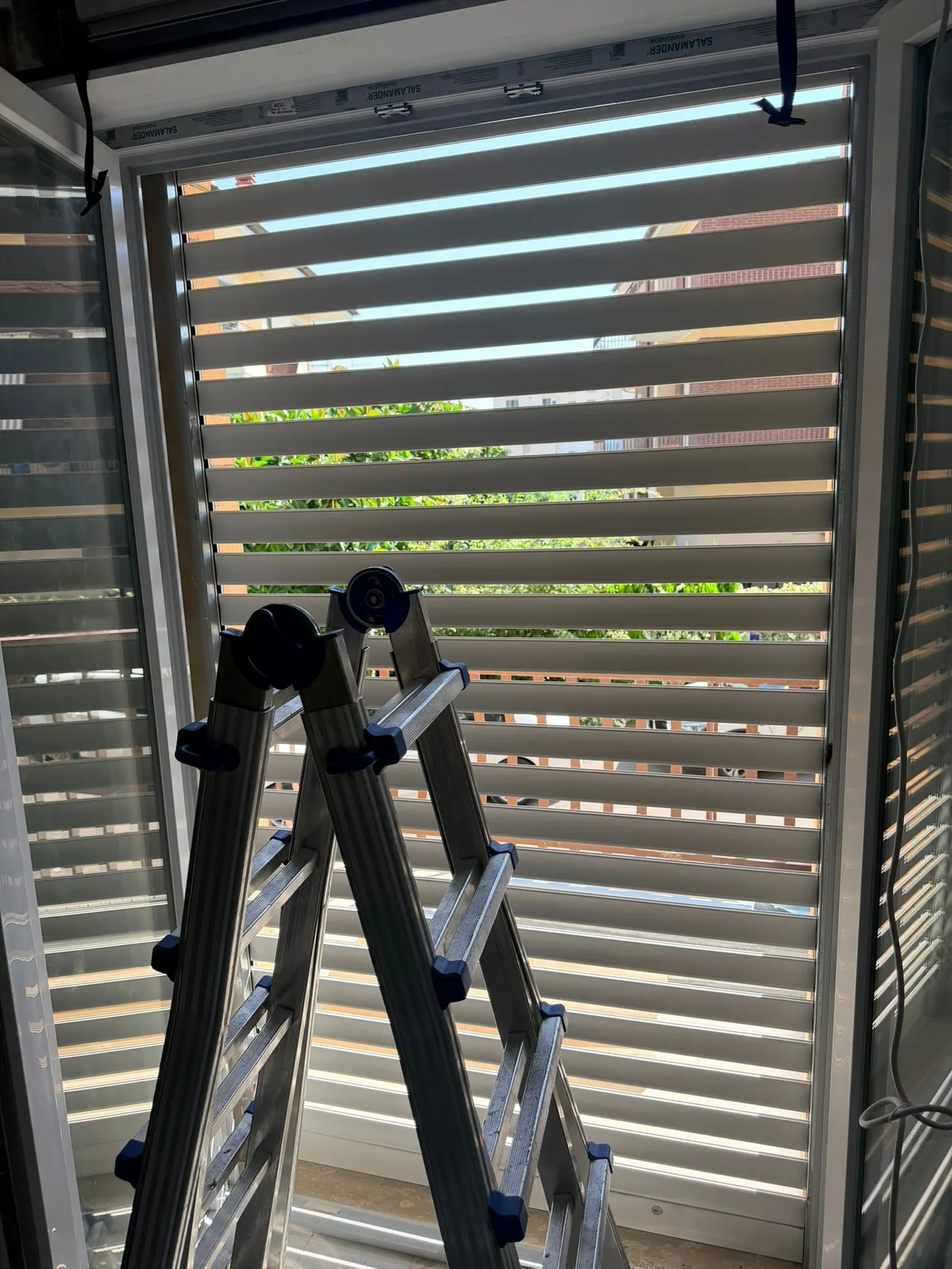 Tapparella a lamelle orientabili semiaperte vista dall'interno durante il montaggio, scala appoggiata davanti