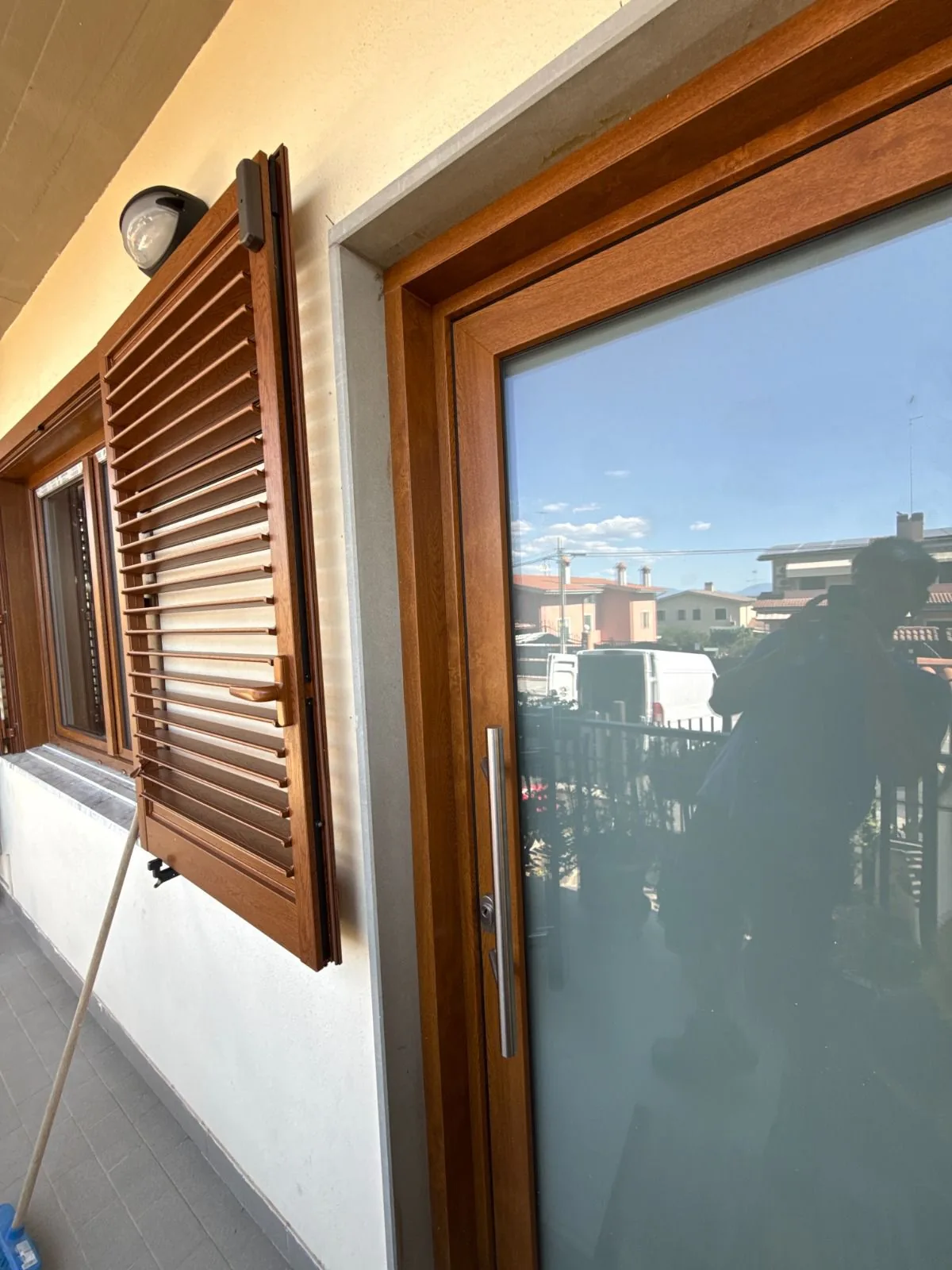 Porta d'ingresso con vetro satinato accanto a una persiana a lamelle, entrambe effetto legno