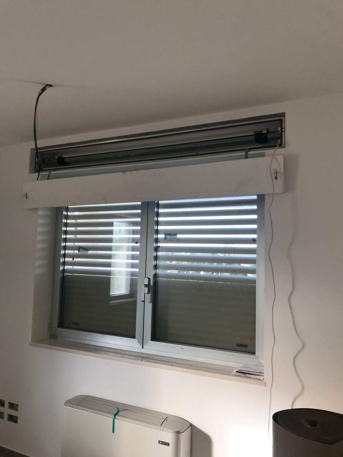 Tapparella blindata Brisolè semiaperta vista dall'interno attraverso una finestra a due ante, con cassonetto aperto in cantiere