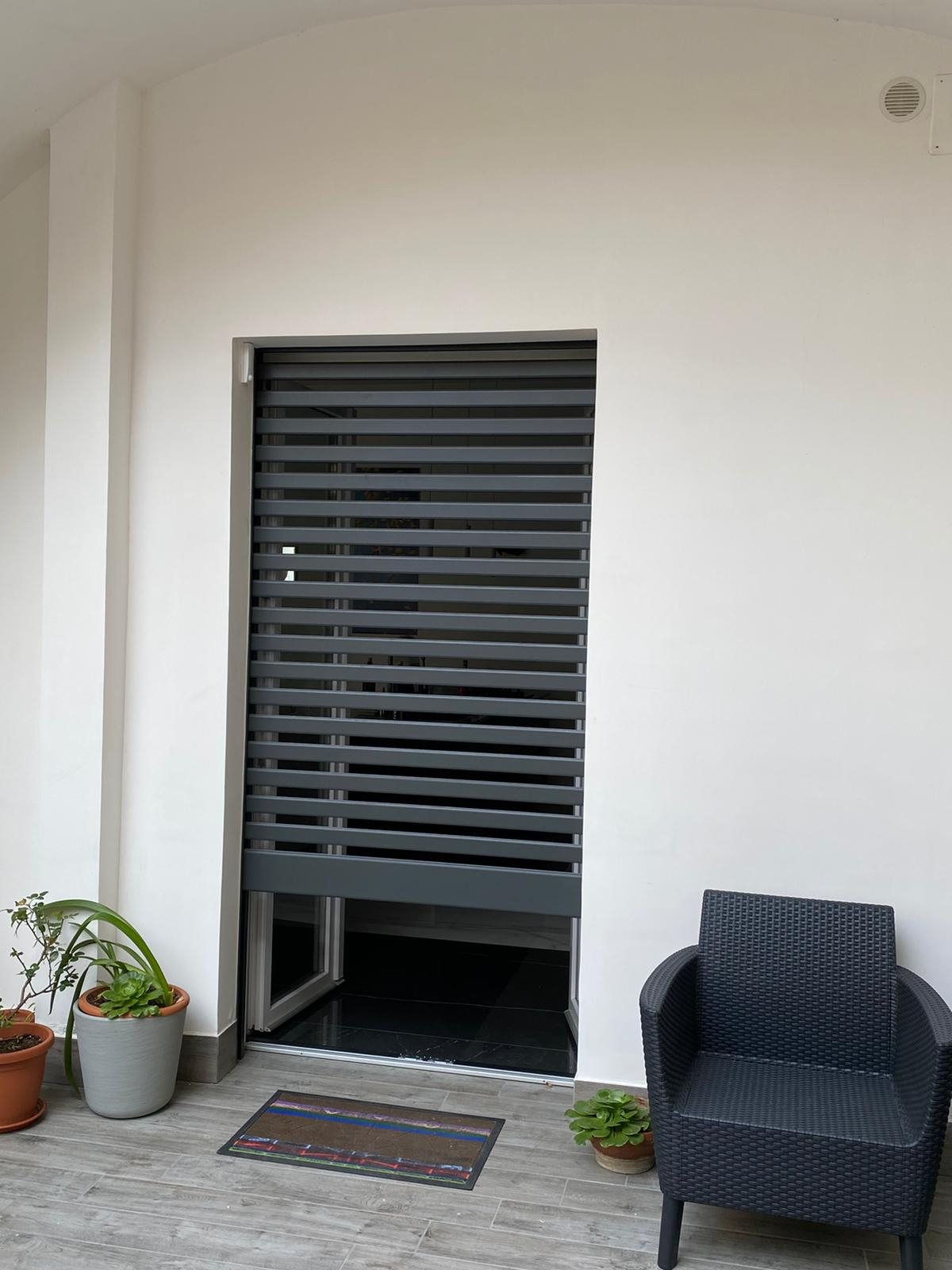 Tapparella blindata Brisolè grigio antracite a doghe distanziate su porta-finestra, vista dal patio