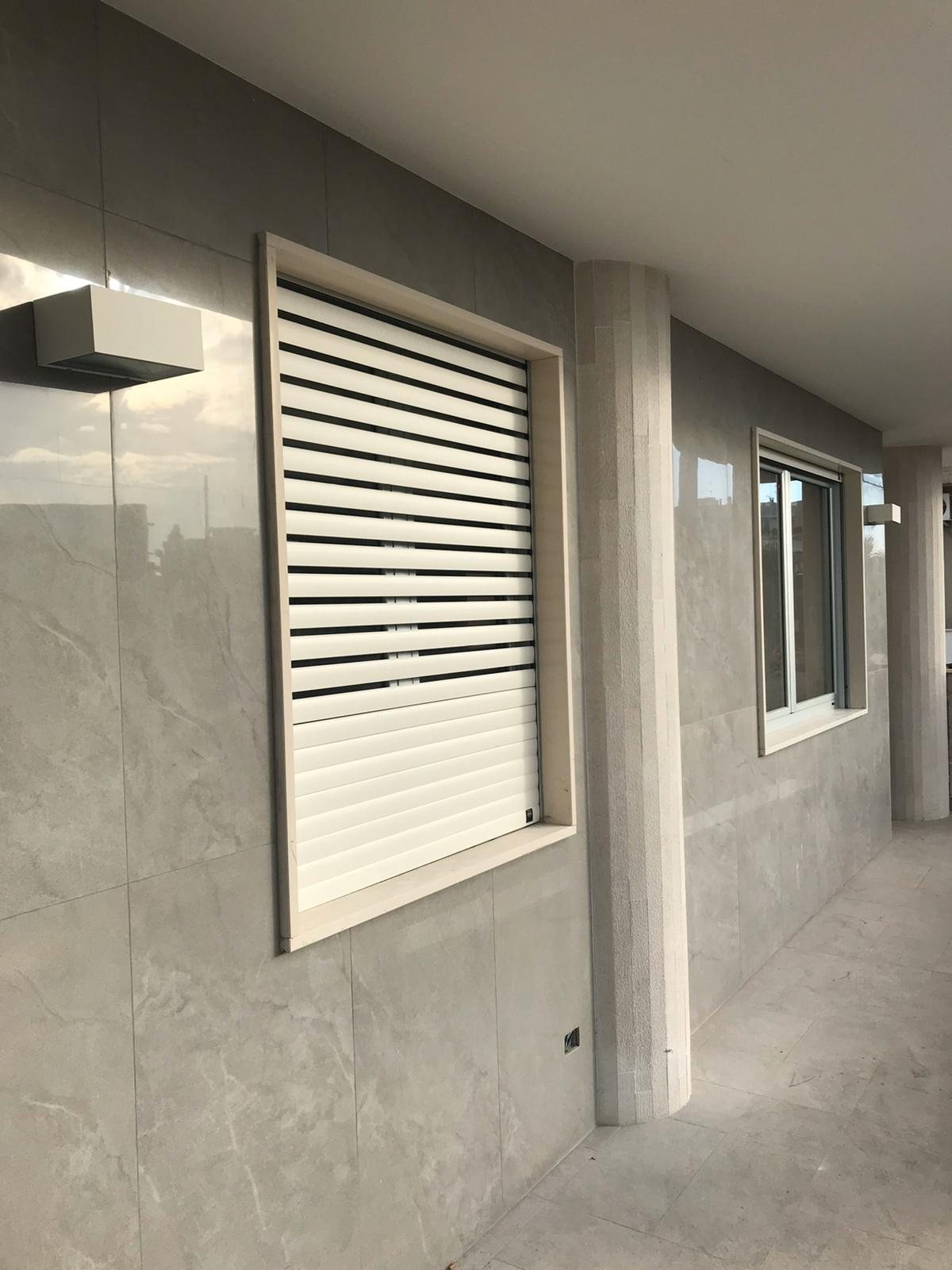 Tapparella blindata Brisolè bianca semiaperta su finestra con rivestimento in gres effetto marmo, vista dall'esterno