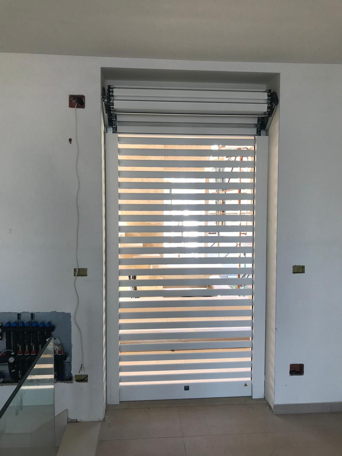 Tapparella blindata Brisolè bianca a doghe distanziate in posa su porta-finestra, cassonetto aperto, vista dall'interno