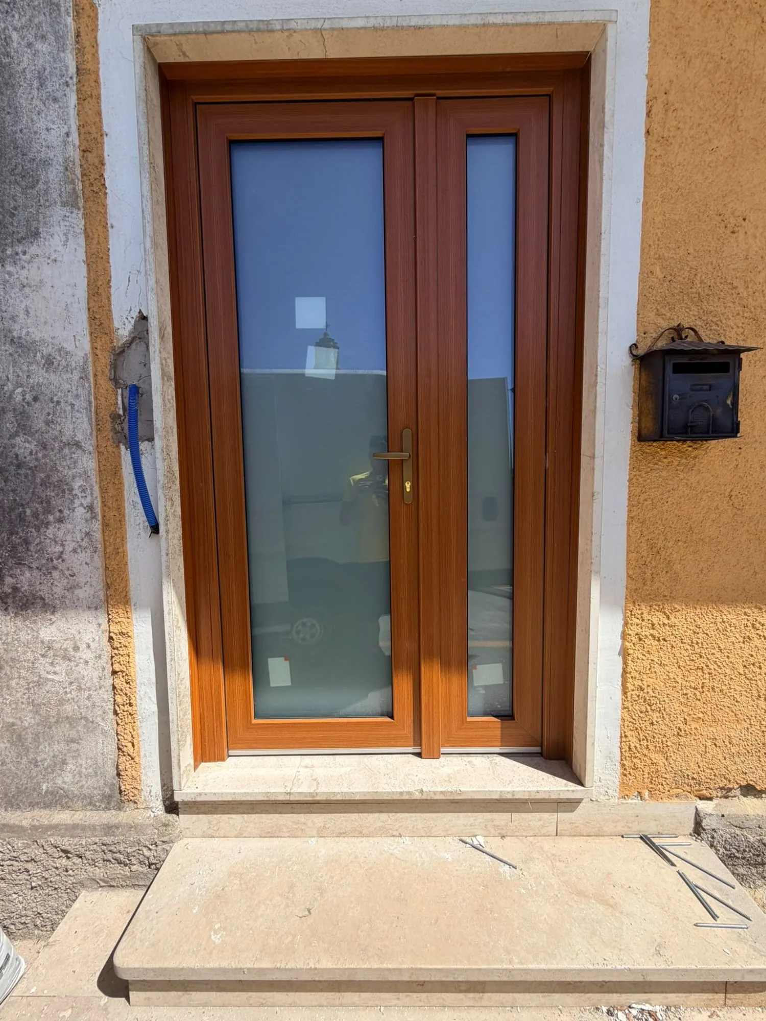 Portoncino d'ingresso in PVC effetto legno a due ante con vetro satinato, cornice in travertino