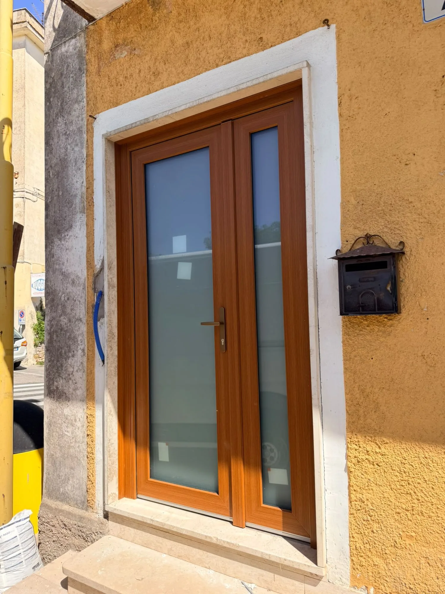 Portoncino d'ingresso in PVC effetto legno con vetro satinato visto di scorcio, cassetta postale in ferro accanto