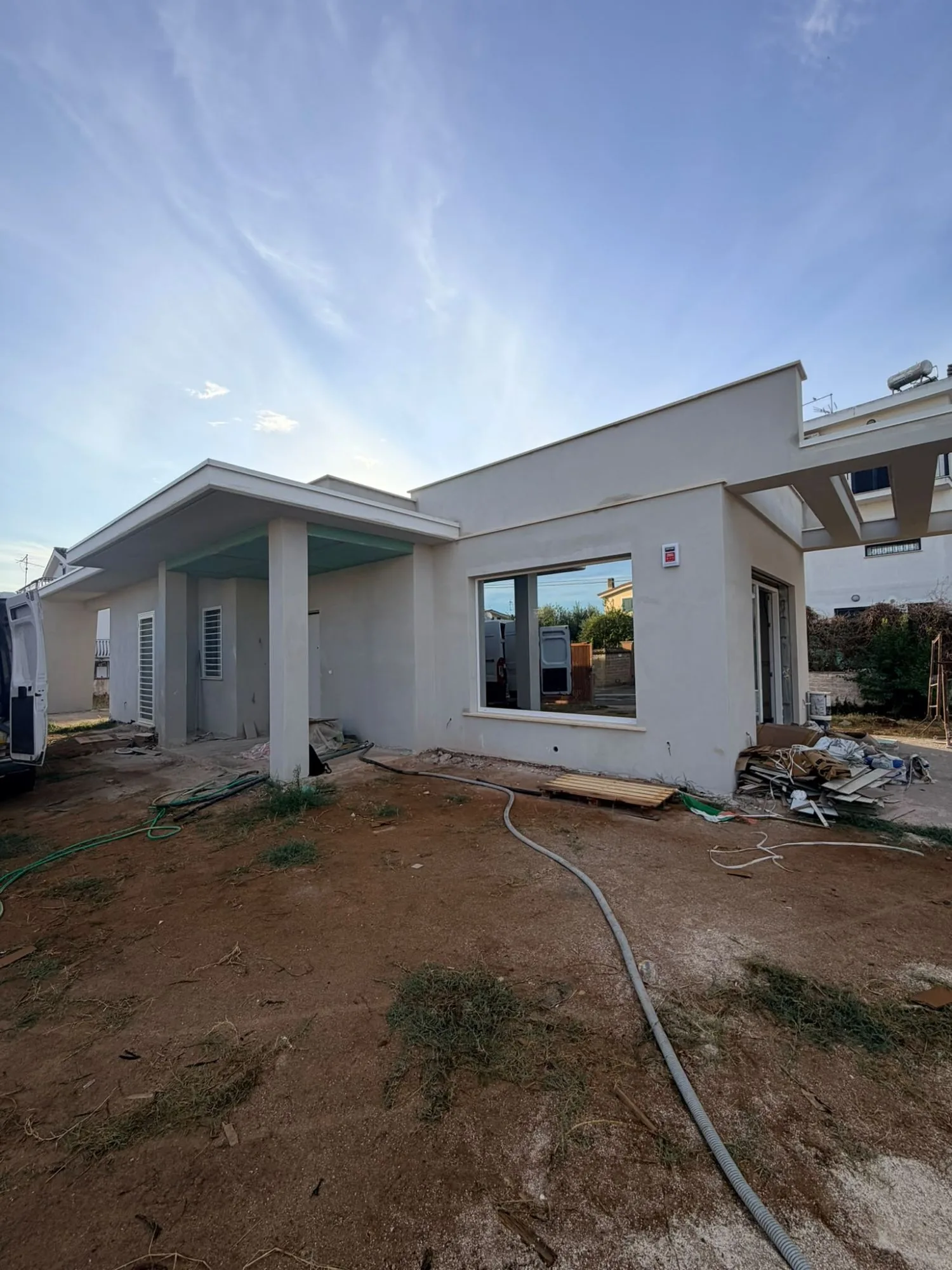 Villa in costruzione con grande finestra fissa a telaio bianco, portico e grate bianche, furgone in cantiere