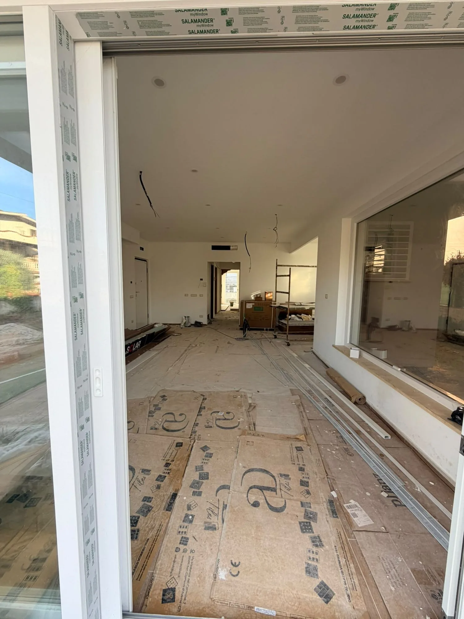 Portafinestra scorrevole in PVC bianco aperta con pellicole Salamander, vista sull'interno di una casa in cantiere