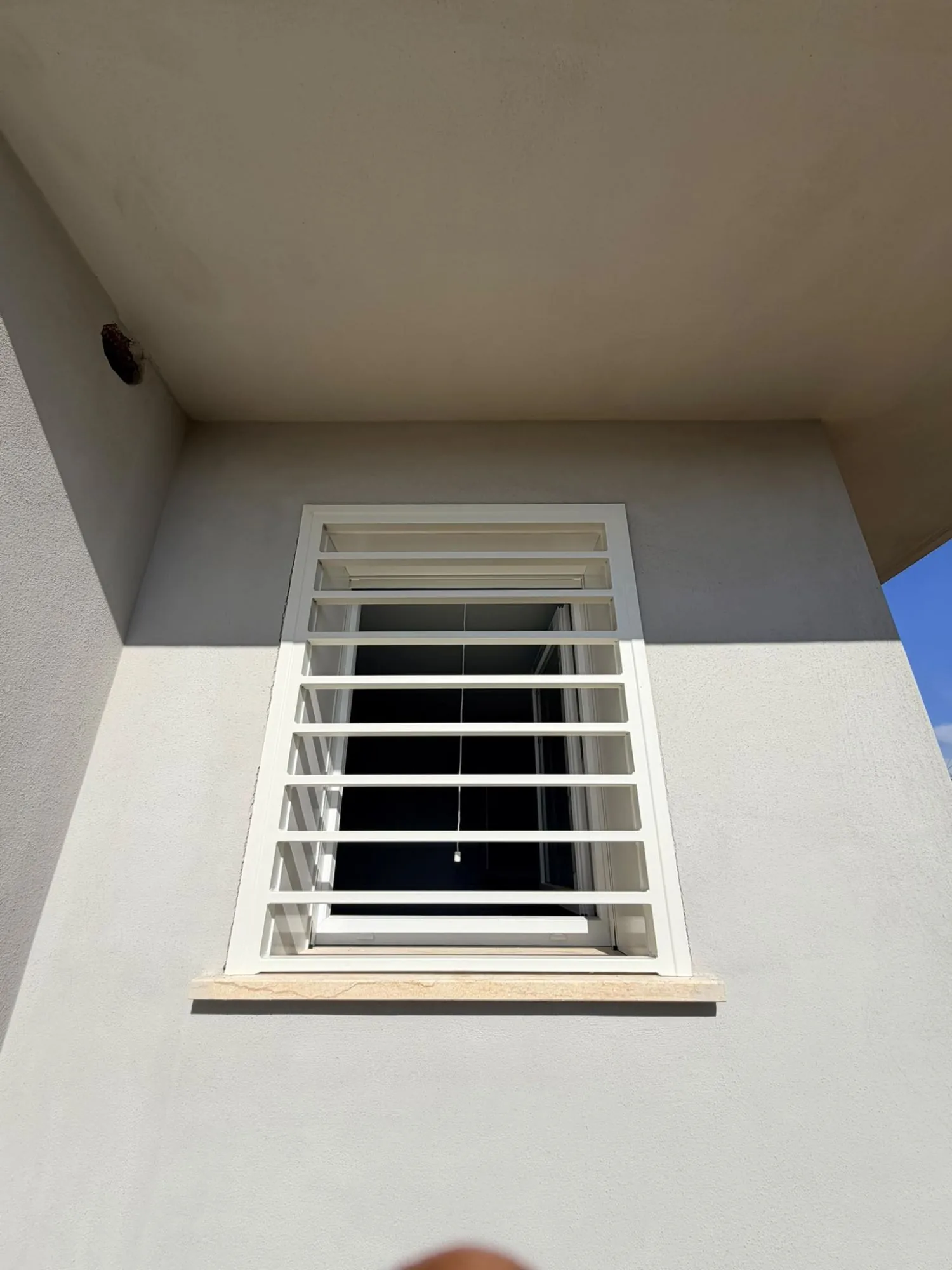 Grata di sicurezza bianca a barre orizzontali su finestra in PVC bianco, vista dal basso sotto lo sporto del tetto