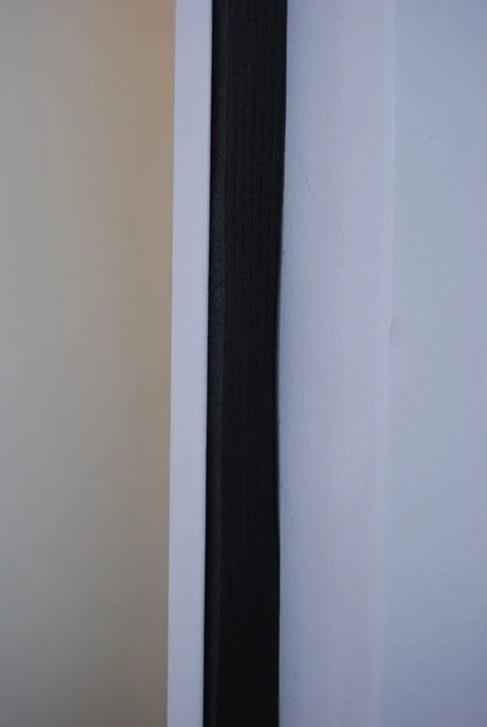 Guarnizione nera continua montata lungo il telaio bianco di una porta metallica, vista in primo piano.