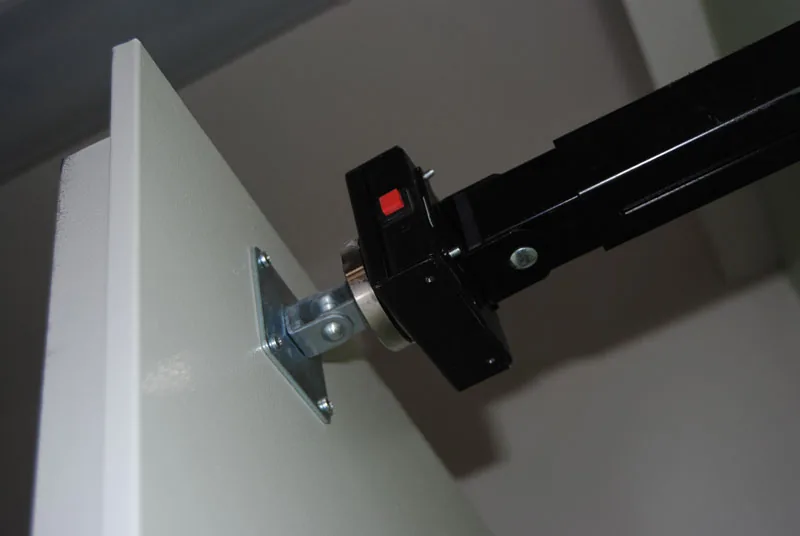 Elettromagnete nero su braccio a muro, con pulsante rosso di sblocco, agganciato alla contropiastra avvitata sull'anta.