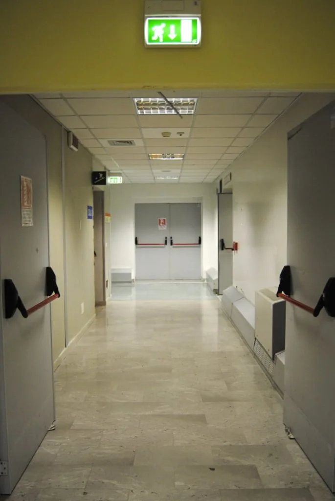 Corridoio con porte metalliche a due ante e maniglioni antipanico ai lati e un'altra porta a due ante in fondo.