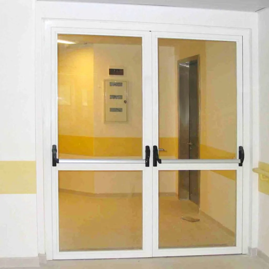 Porta vetrata tagliafuoco a due ante chiusa, con profili bianchi, traverso a metà e maniglioni antipanico.