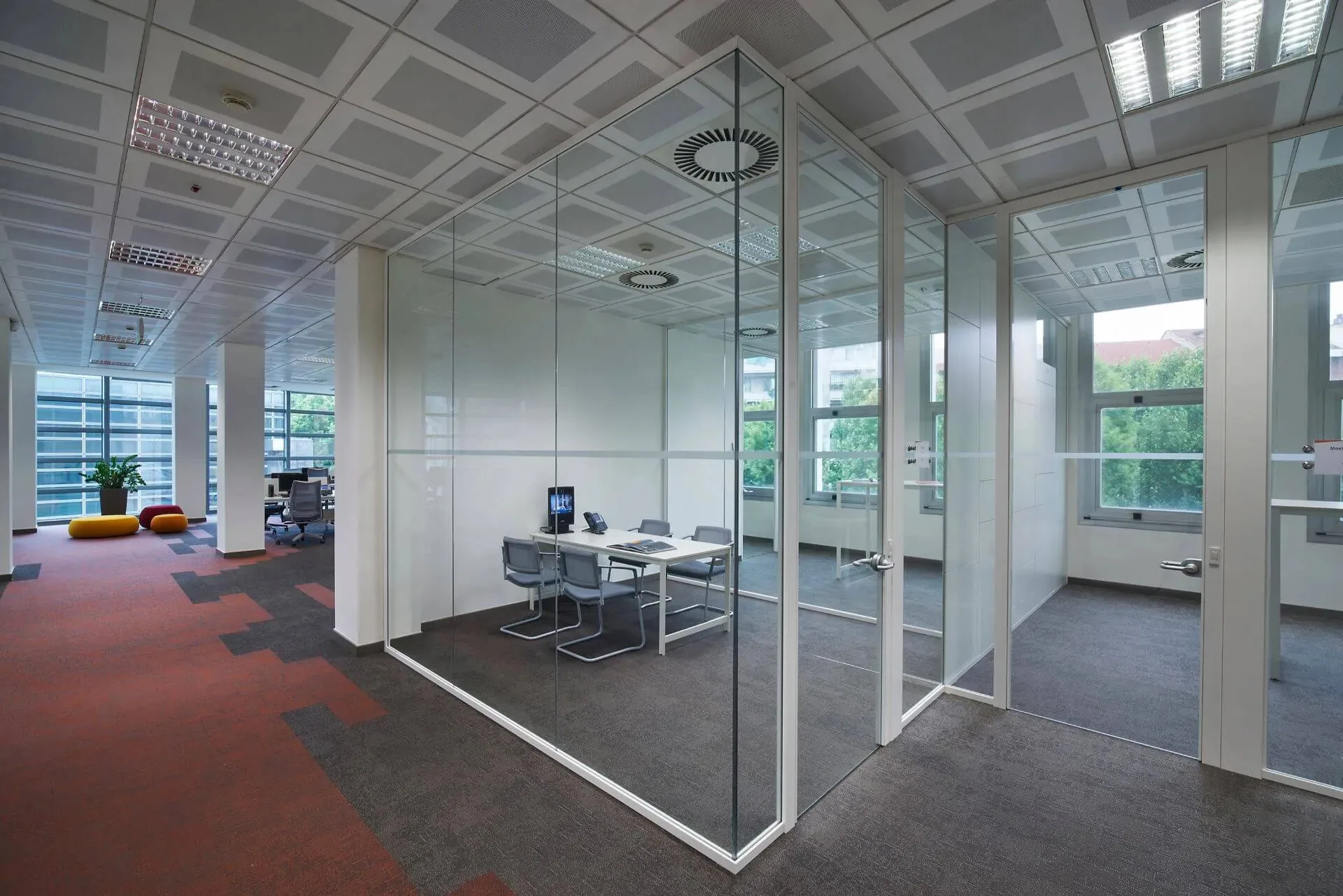 Sala riunioni chiusa da pareti TRUELIGHT in vetro con profili bianchi e porte vetrate in un open space con moquette