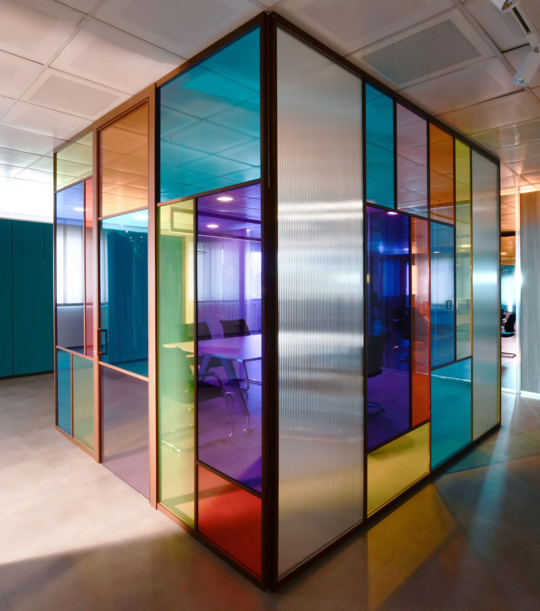 Sala riunioni chiusa da pareti con vetri colorati turchese, viola, giallo e arancio e profili color bronzo
