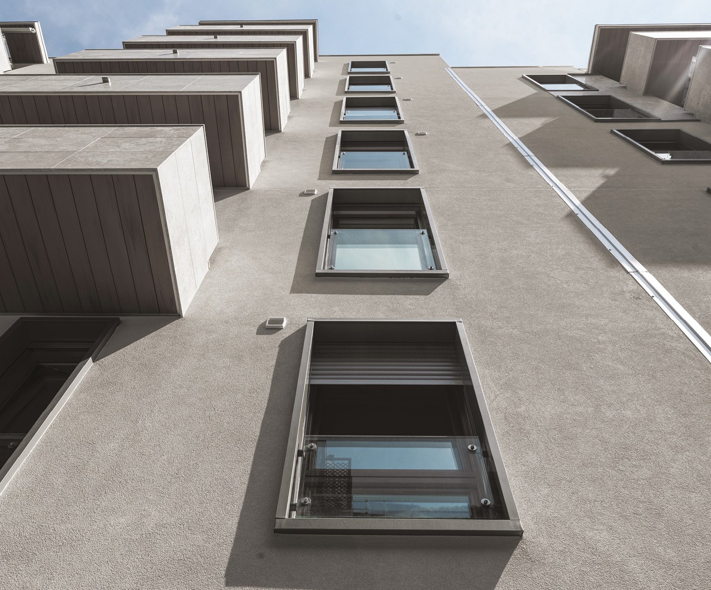 Facciata di un palazzo moderno fotografata dal basso verso l'alto: una fila verticale di finestre scure con parapetto in vetro
