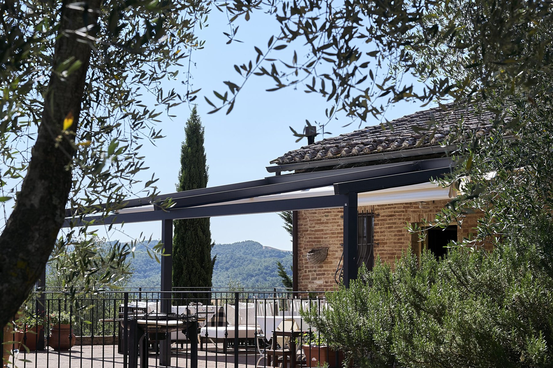 Casale in mattoni con la terrazza coperta da una pergola antracite a telo chiaro