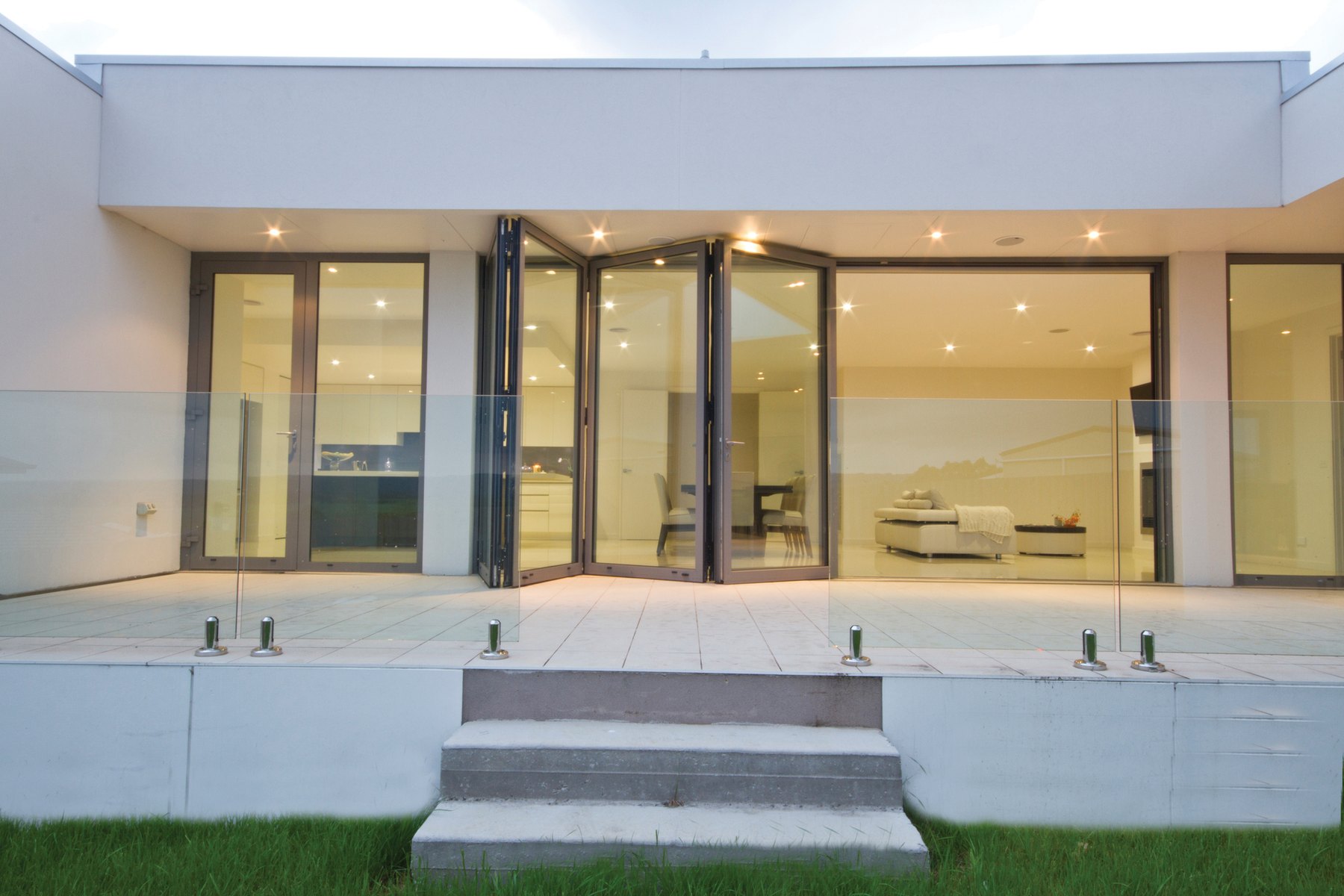 Villa all'imbrunire con portefinestre a libro aperte sul soggiorno illuminato